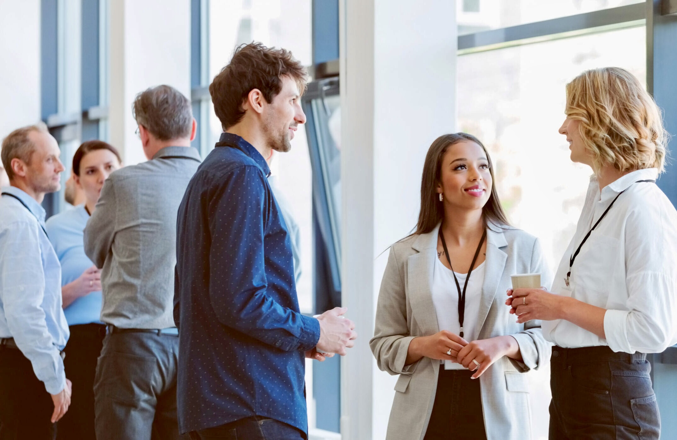 Multiracial group of entrepreneurs discussing during coffee break at business seminar. Group of people standing and talking in the corridor of a business center. Networking concept.